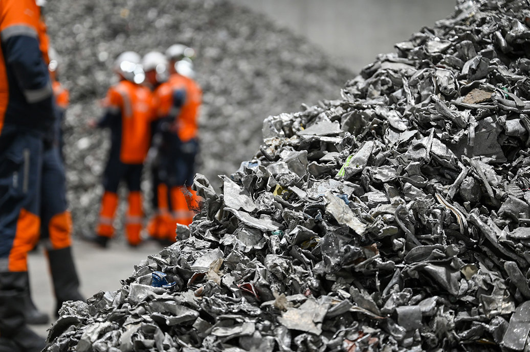 a group of workers in orange vests standing next to a pile of aluminium scrap a group of workers in orange vests standing next to a pile of aluminium scrap